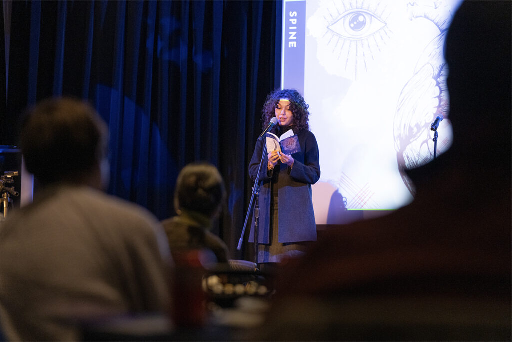 A person reads their work from a stage