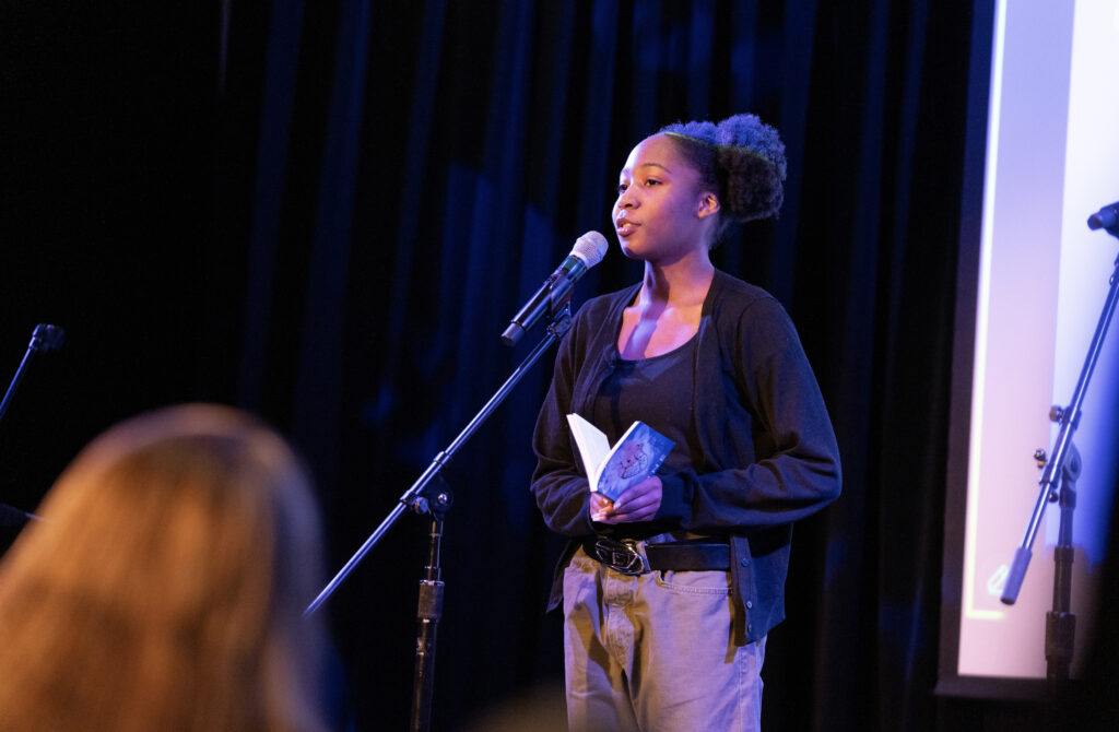 A person stands in front of a mic reading their work to the audience