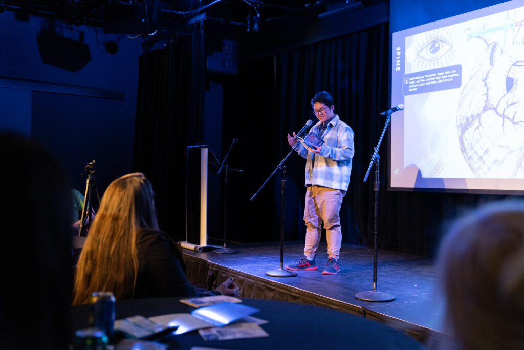 A person reads their work from on stage