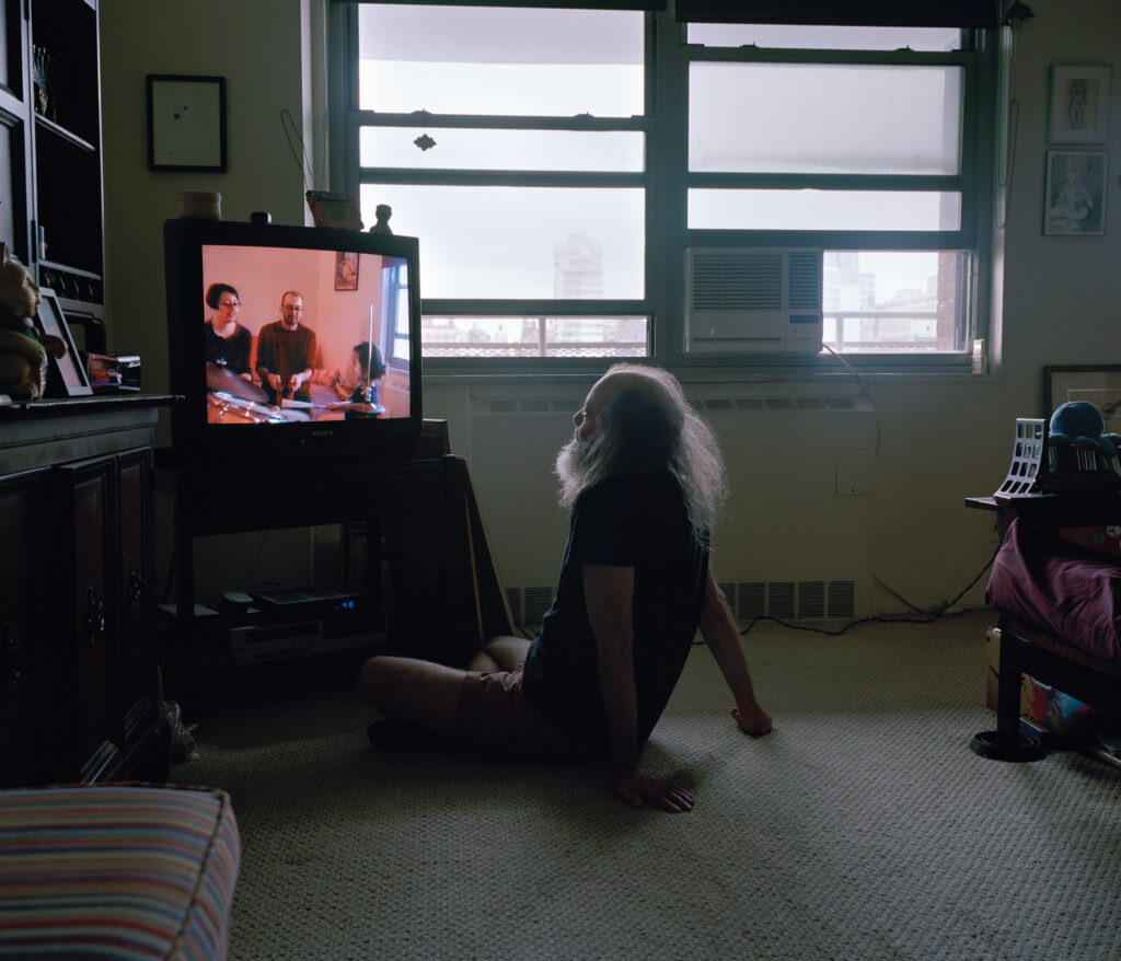 A man watches a home video on tv while sitting on the floor.