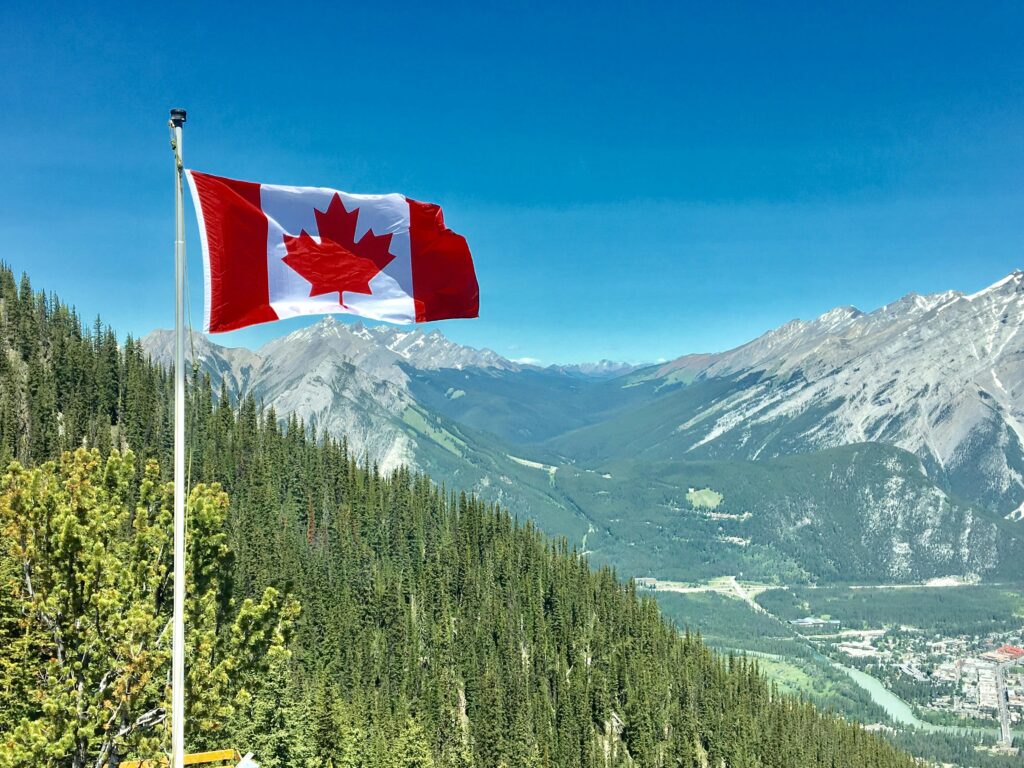 A Canadian flag flying with green and snow-capped mountains in the background