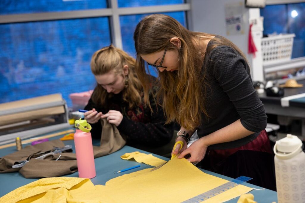 Two students sew and cut fabric