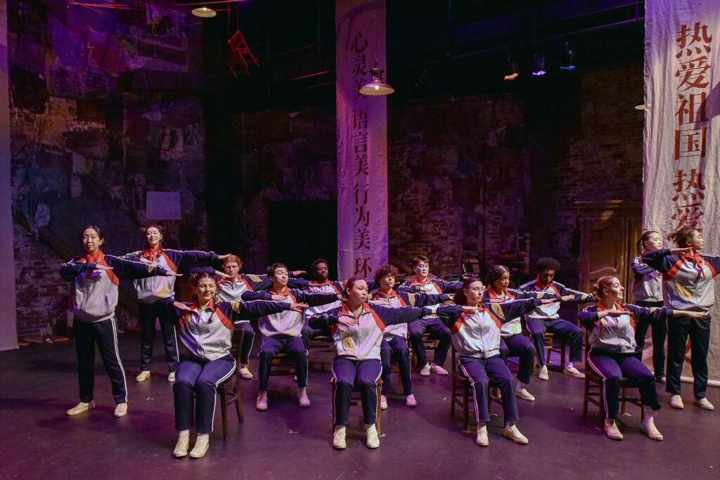 Actors on stage wear track suits while making the same dab motion