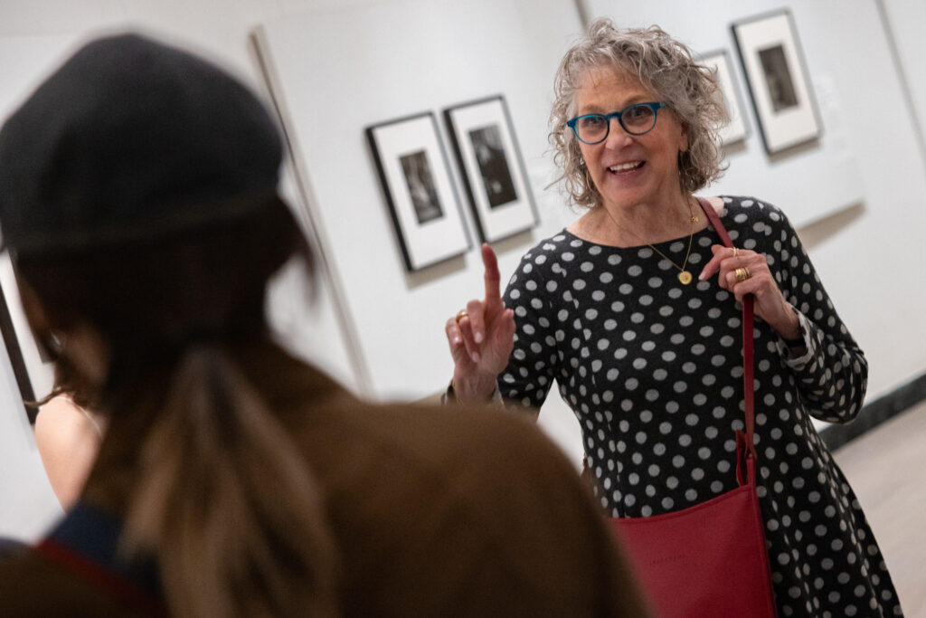 Lauren Shaw smiles while holding up one finger and talking to a student in an art museum