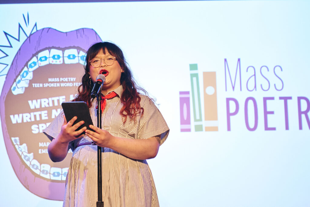 A person reads from a notebook in front of a microphone