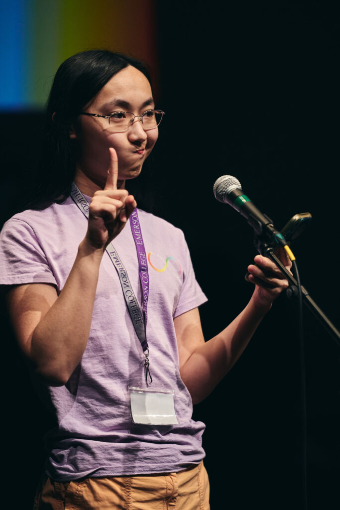 One person holds up one finger and a cellphone in the other hand while in front of a microphone