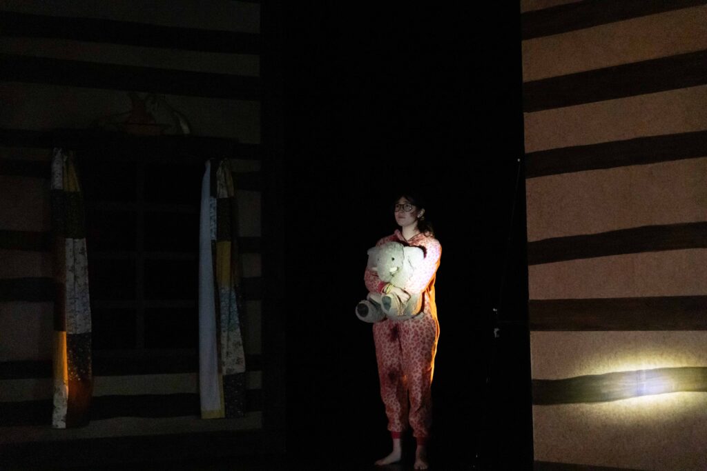A person holds a teddy bear in th dark with a spotlight on them