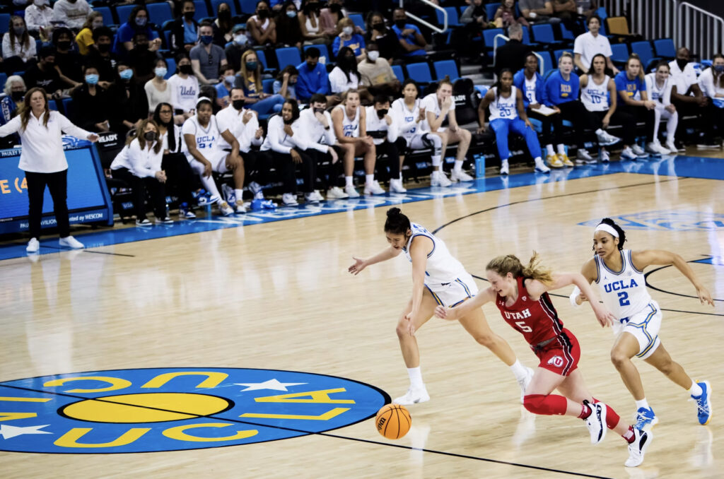 A womens basketball player dribbles away from two teammates