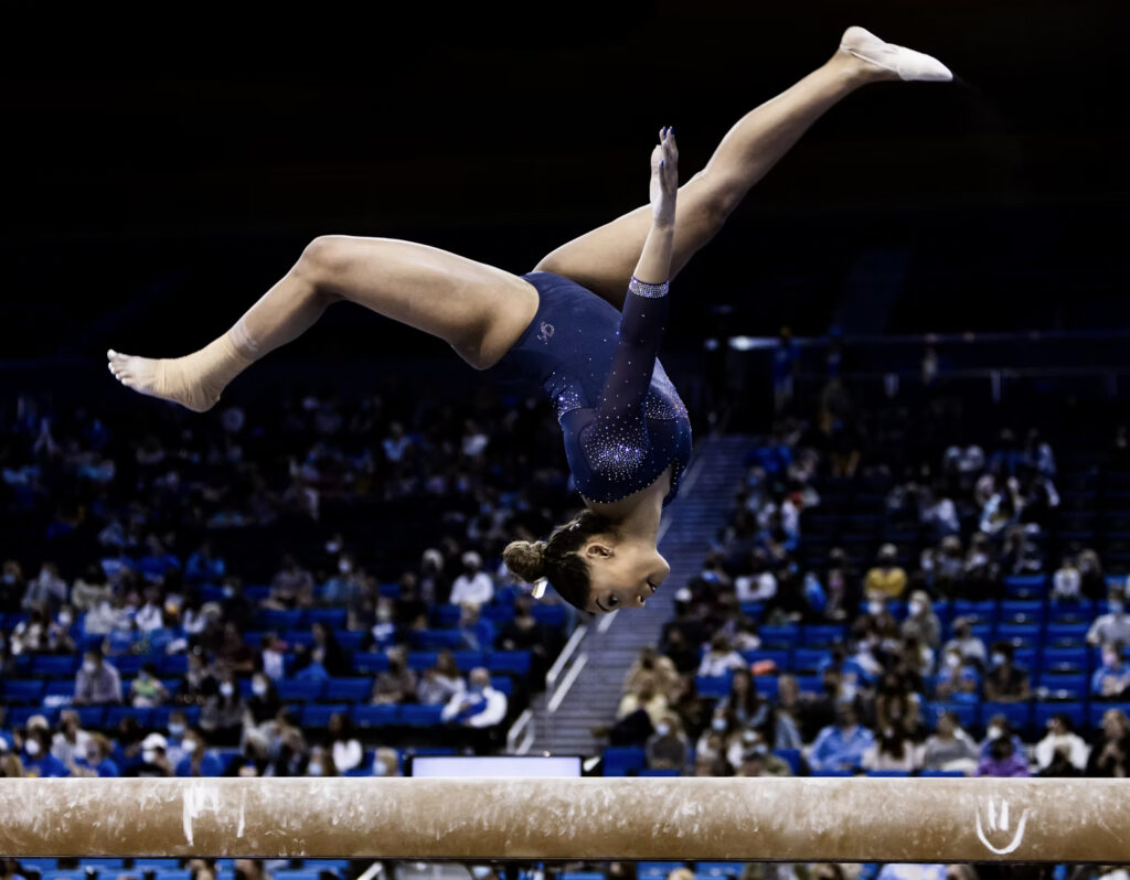 A female gymnast flips upside on the beam