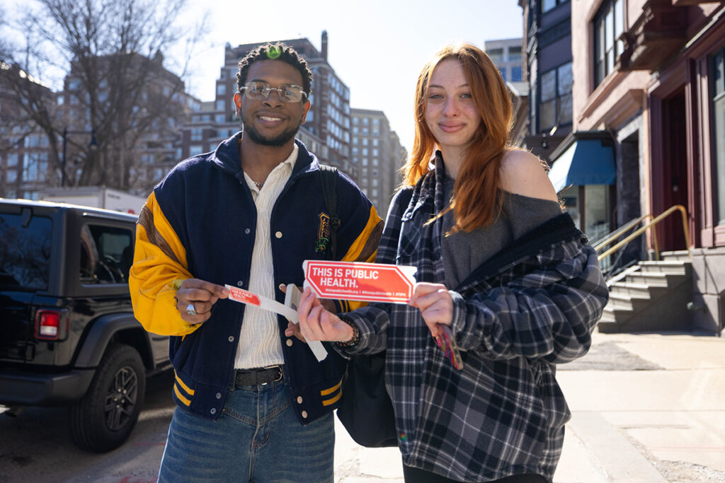 Two people hold up stickers that say This Is Public Health