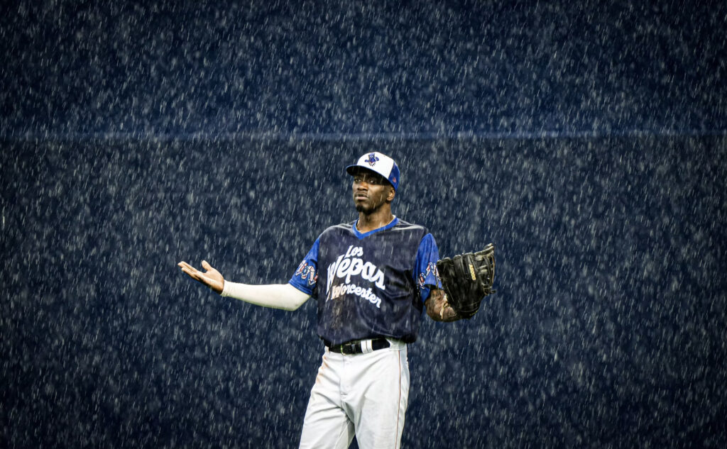 A baseball player lift his arms up as rain comes pouring down