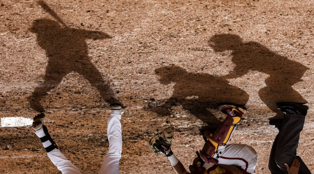 Shadows baseball players are seen in the dirt while players are at home plate