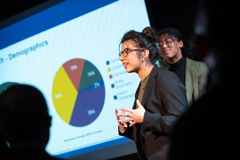 Young woman in black blazer stands in front of a pie chart