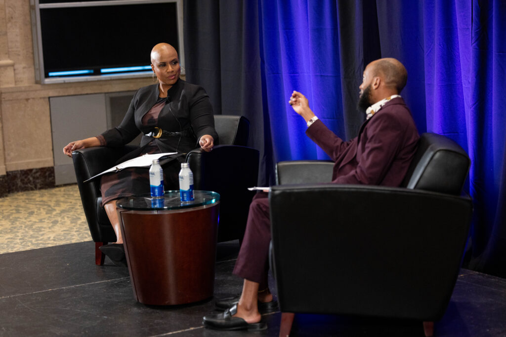 Ayanna Pressley sits while talking to Deion Hawkins.
