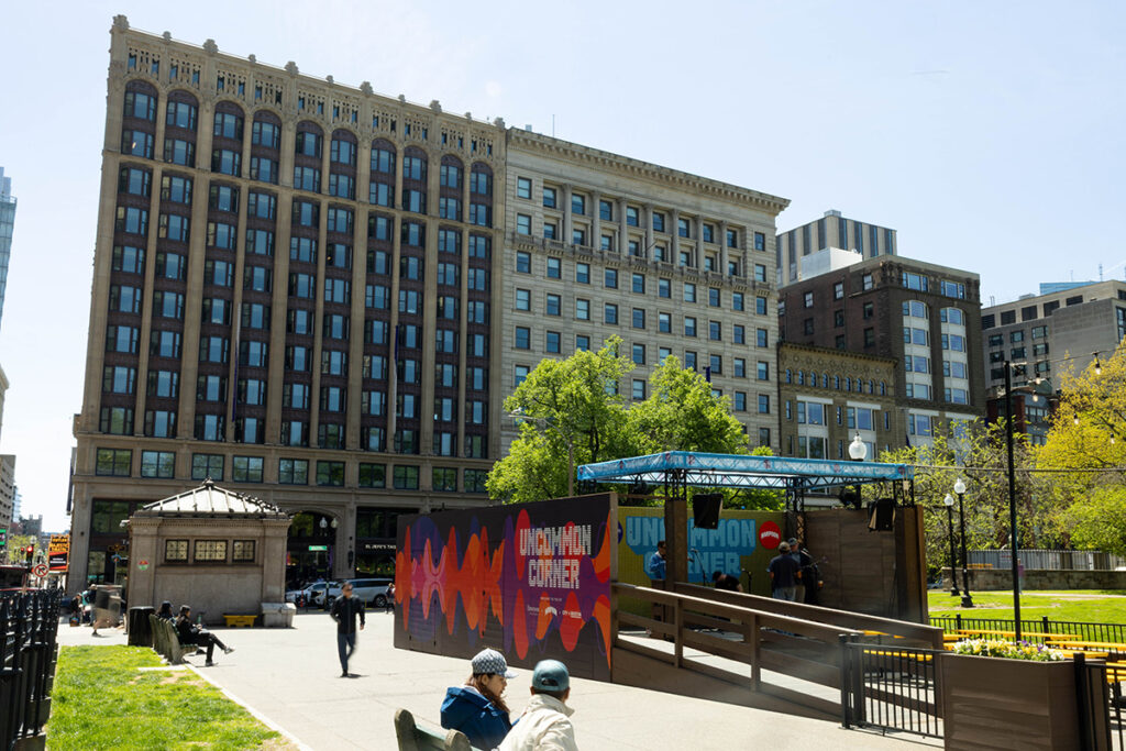 Stage with "uncommon corner" spelled out in bottle caps on the back wall, Emerson campus in the background