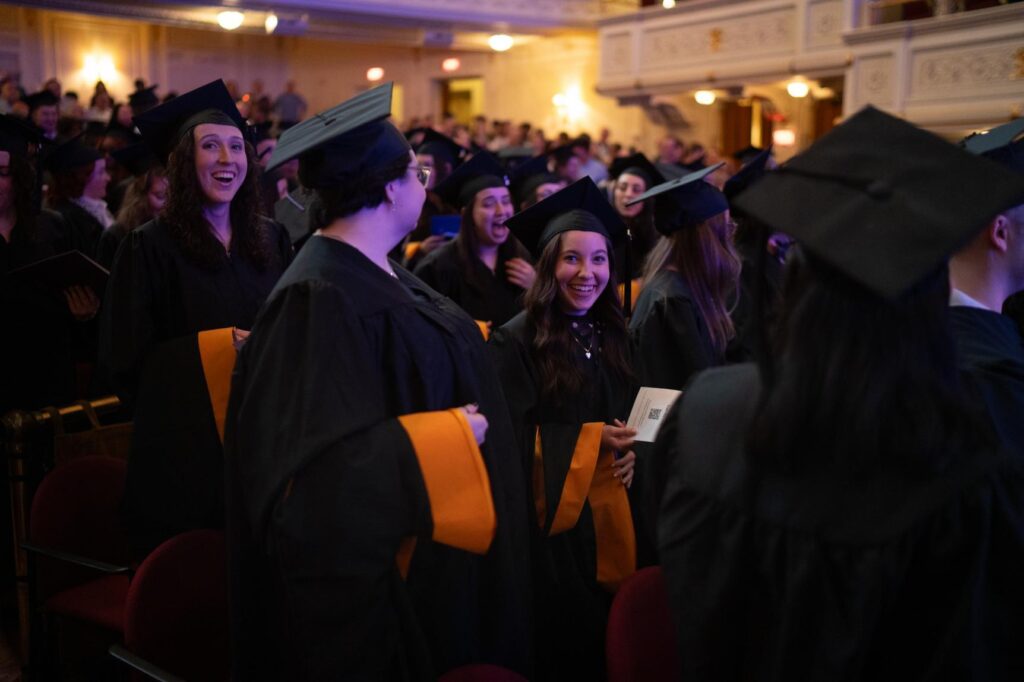 Graduates in cap and gowns sit in the theater