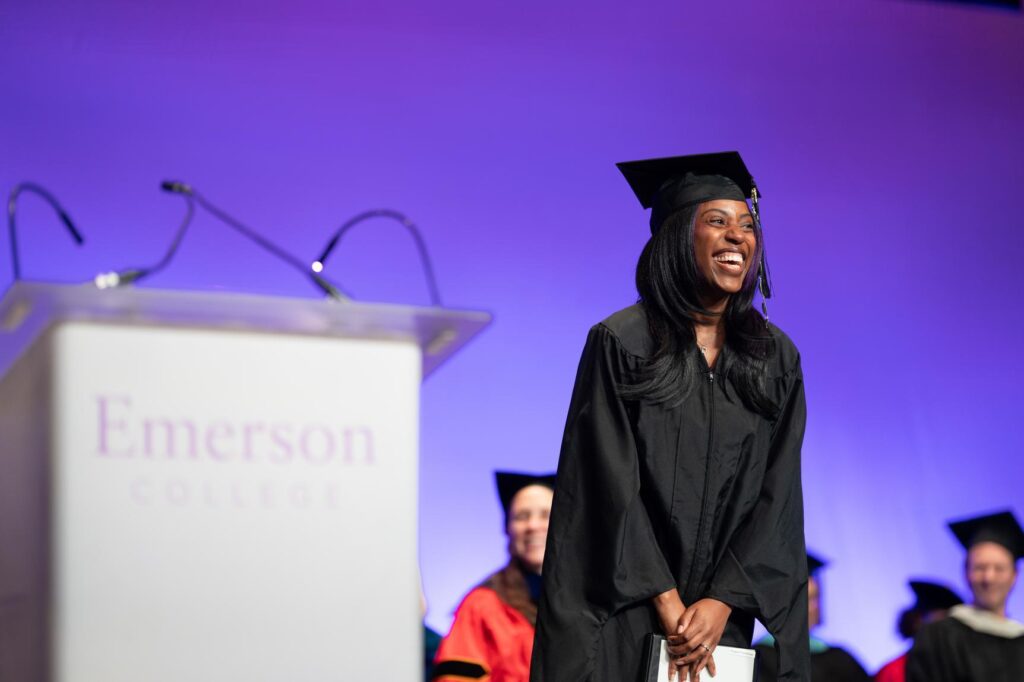 a woman smiles in a cap and gown on stage