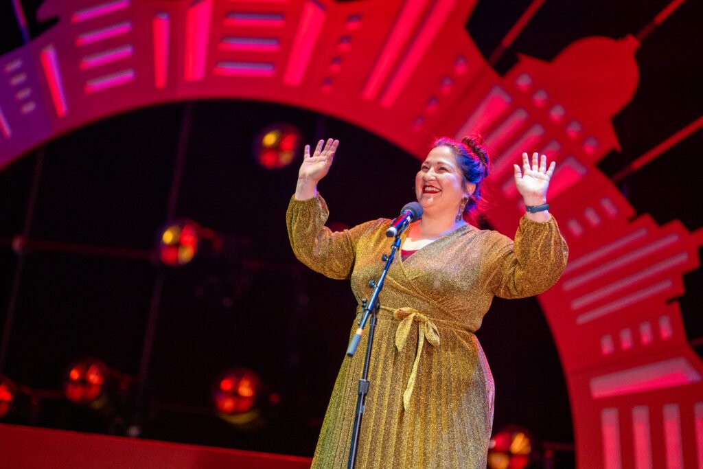 A person holds up their hands in the air while talking at the microphone on stage