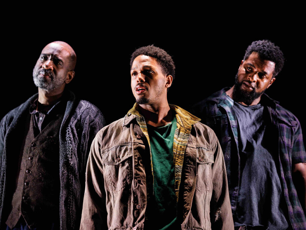 Three black men in plaid shirts, denim jackets look off camera