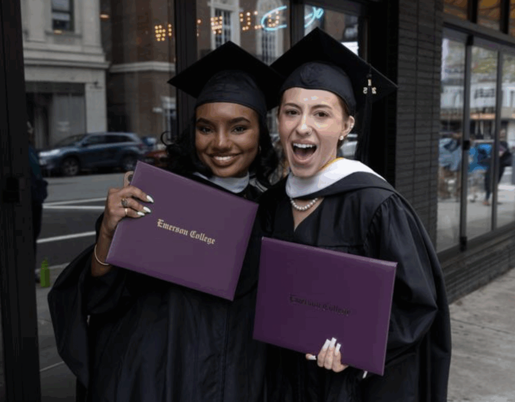 Two graduates hold their diplomas and smile for the camera