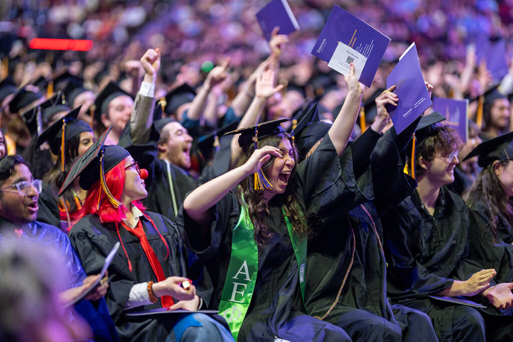 Seated students in caps and gowns cheer
