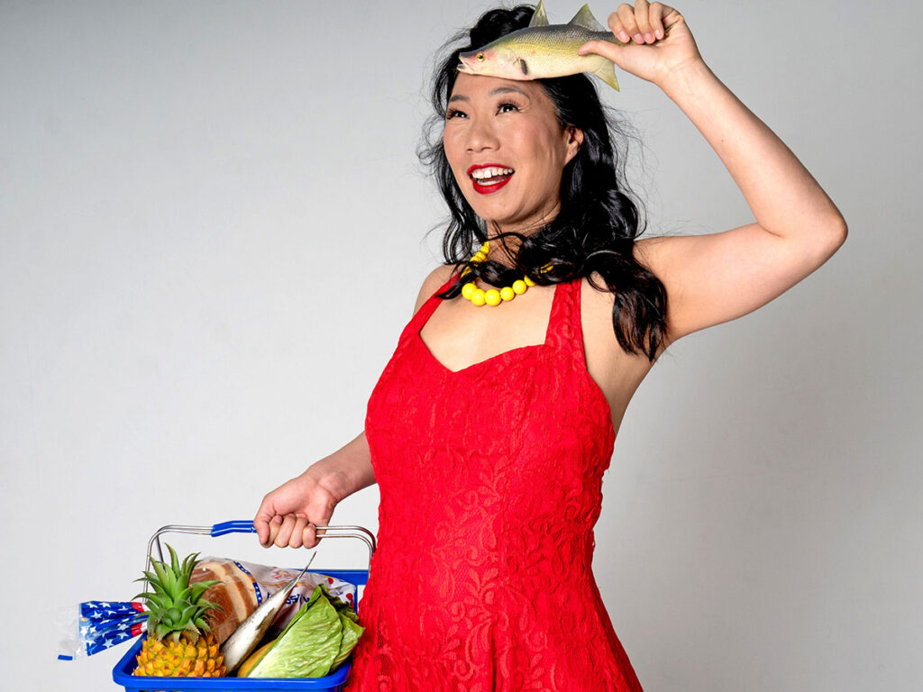 woman in red dress holding basket of groceries salutes with a fish