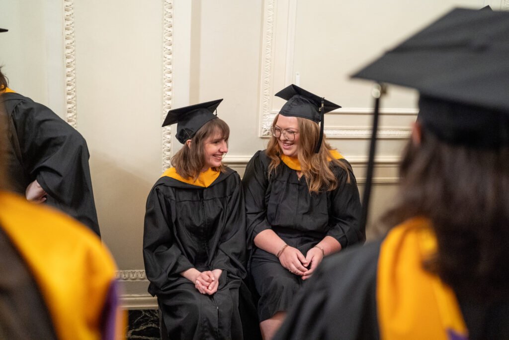 Two grads sitting next to each other and smiling.