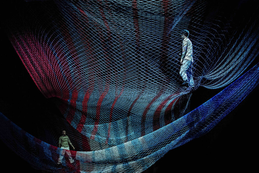 Two performers walk inside colorful nets suspended from ceiling