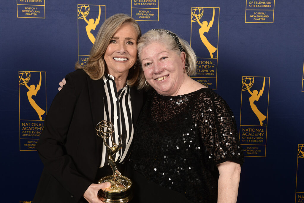 Two women side hug, one holds Emmy