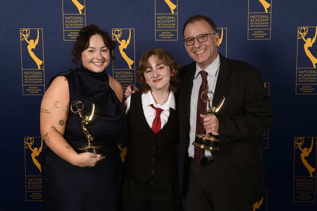 Two adults hold Emmys with young adult between them