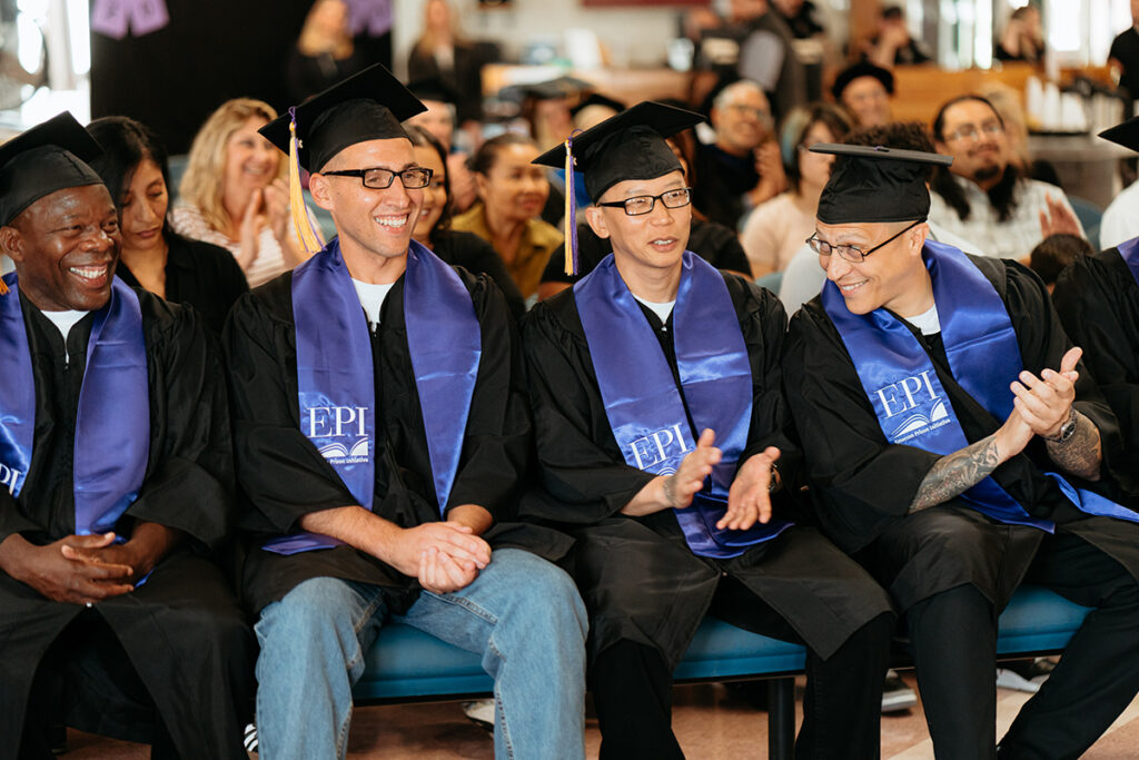 Men in caps and gowns sit in a row clapping