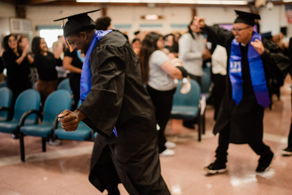 Two men in caps and gowns dance in an aisle