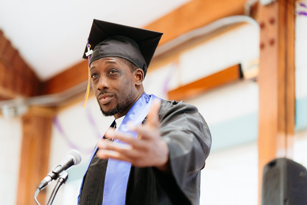 Man in cap and gown gestures behind podium