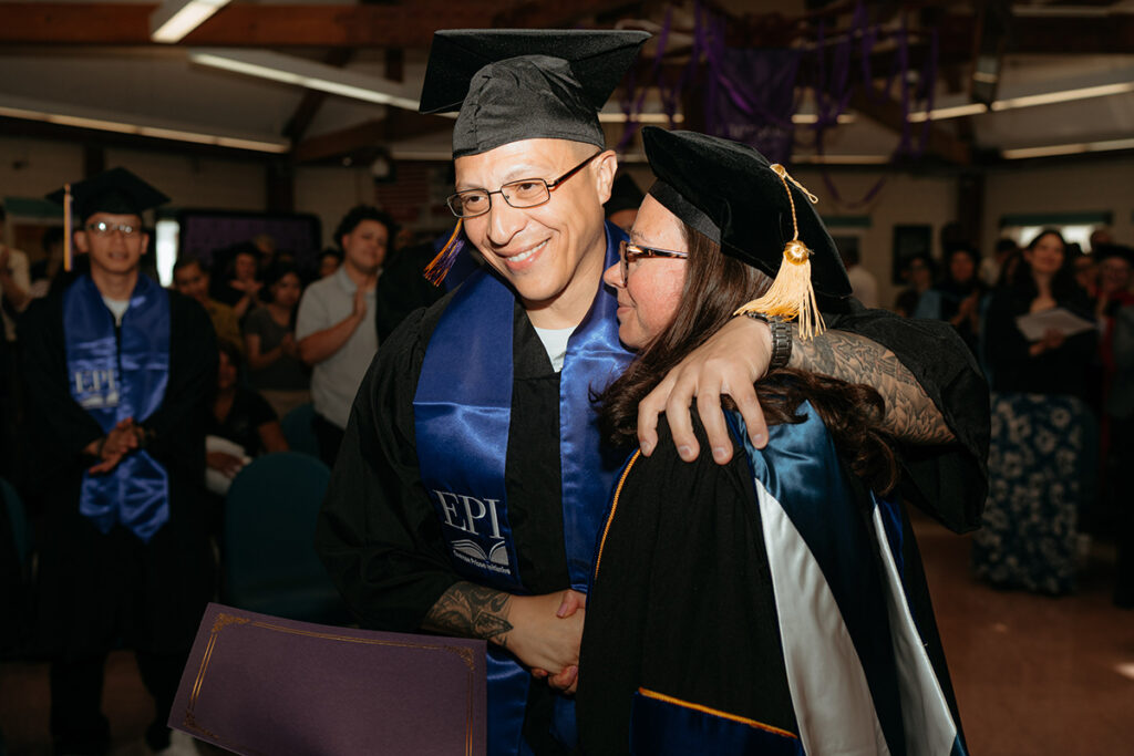 Man in cap and gown hugs woman in academic regalia