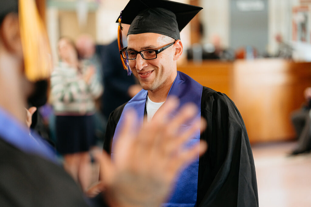 Man in cap and gown smiles as classmates hold out hands