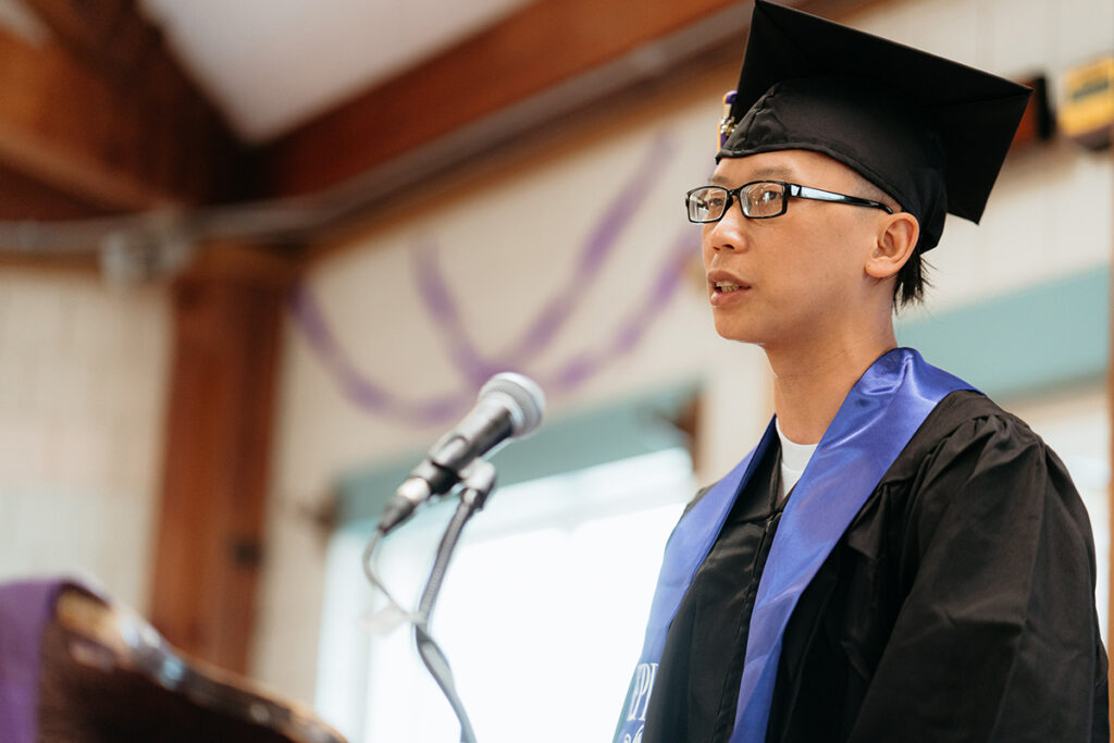 man in cap and gown speaks at podium