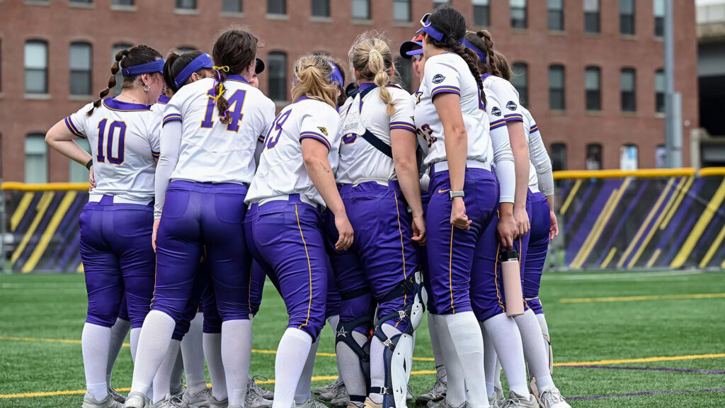 Softball players put their hands in together in a huddle