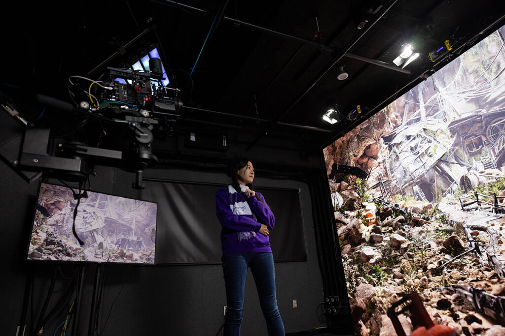 Woman stands before a large screen showing a fantastical scene