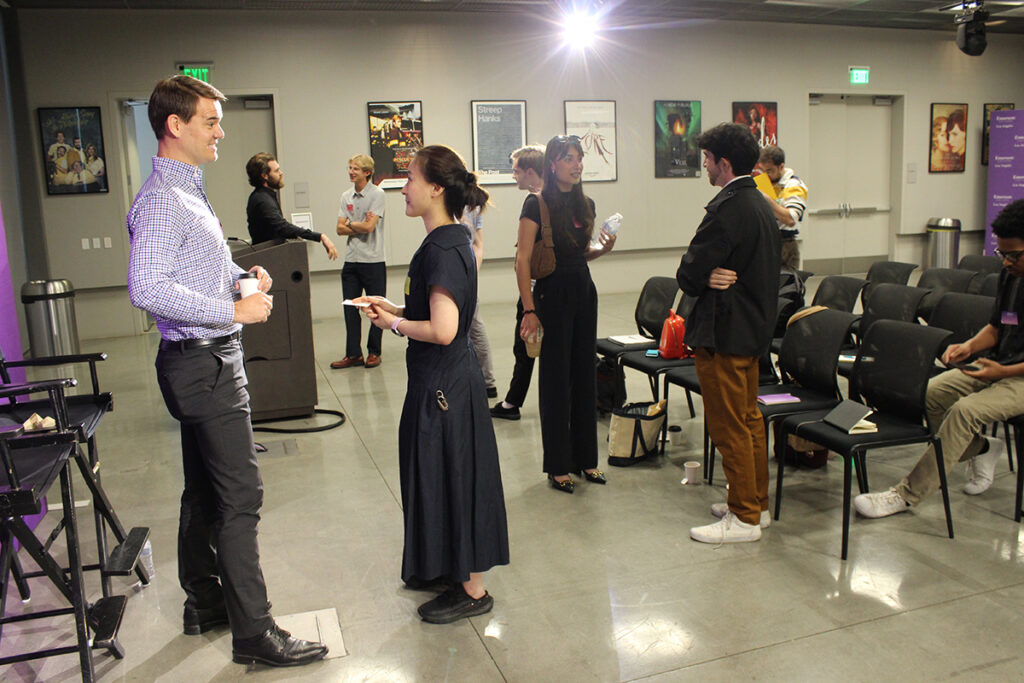 Man in checked shirt talks to woman in black dress in room at ELA