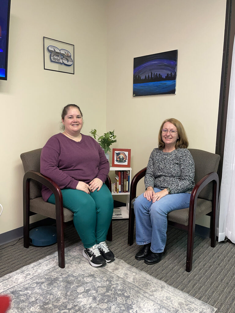 Two women sit in chairs with hands in lap