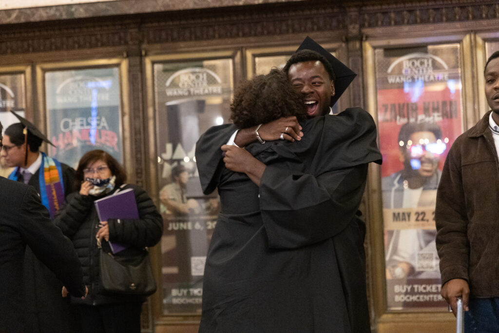 A person hugs another person, both in graduation gowns