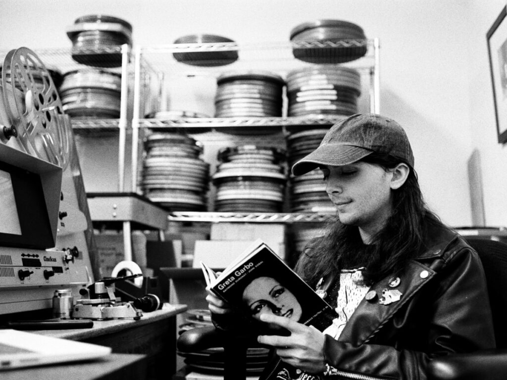 Jordan Marshall reading a book about Garbo in front of stack of film reels