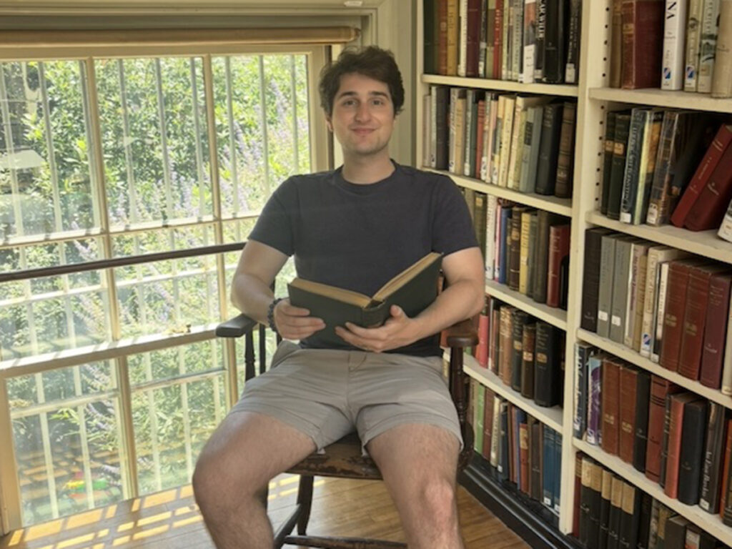 Matt Albren holding an open book in front of a window, book shelves