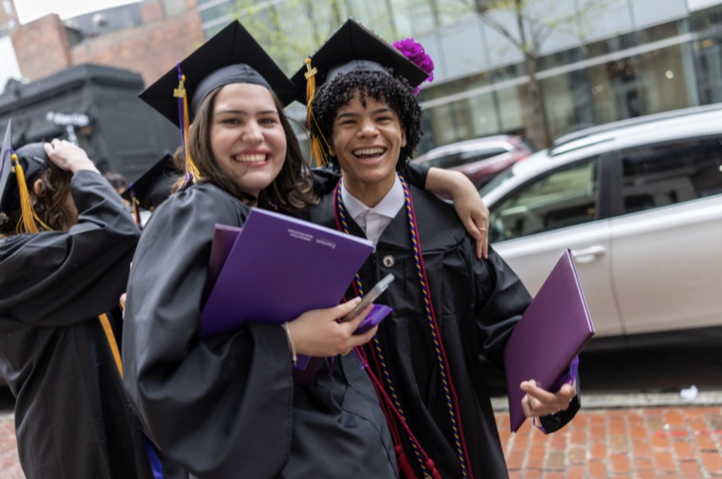 Two people stand together with their diplomas