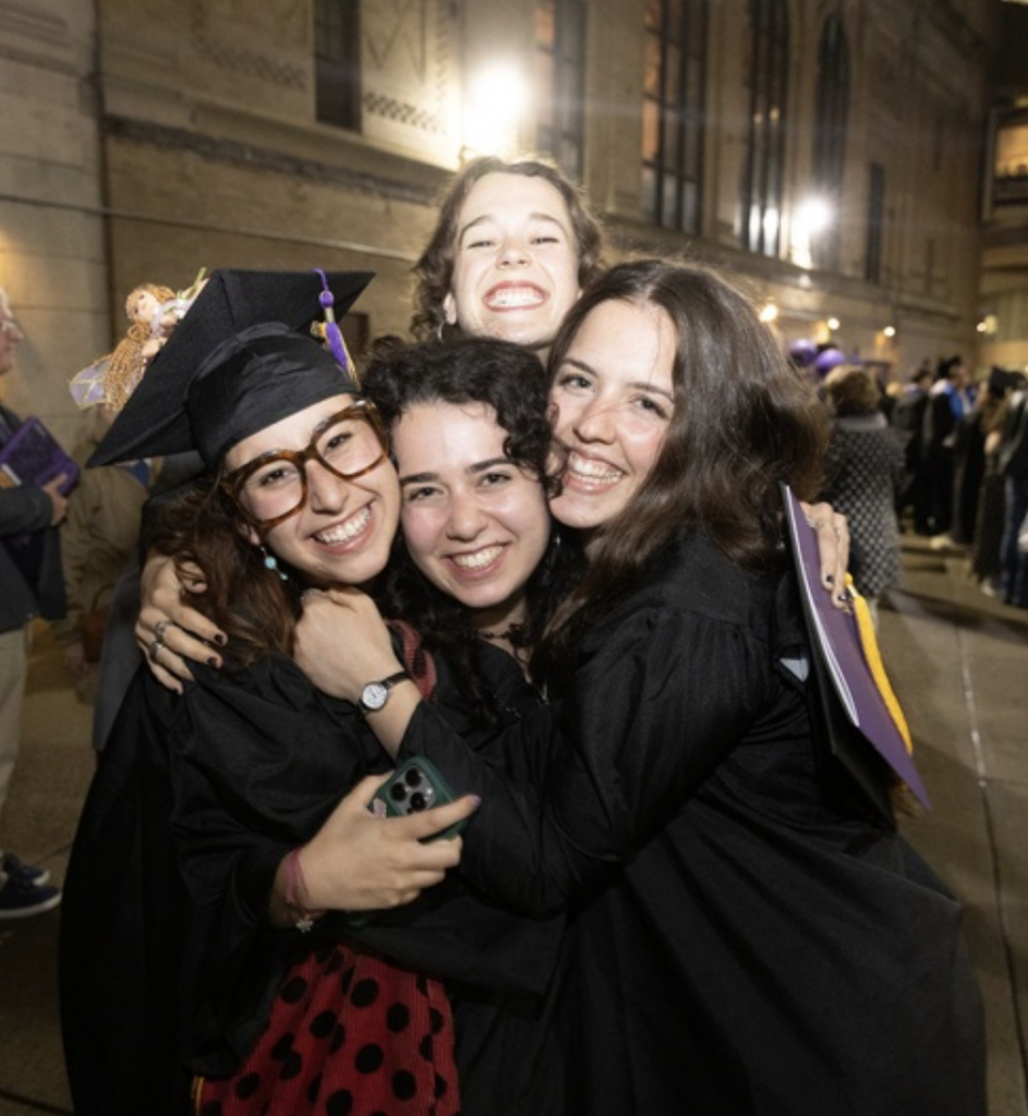 Four students hug each other while smiling for the camera