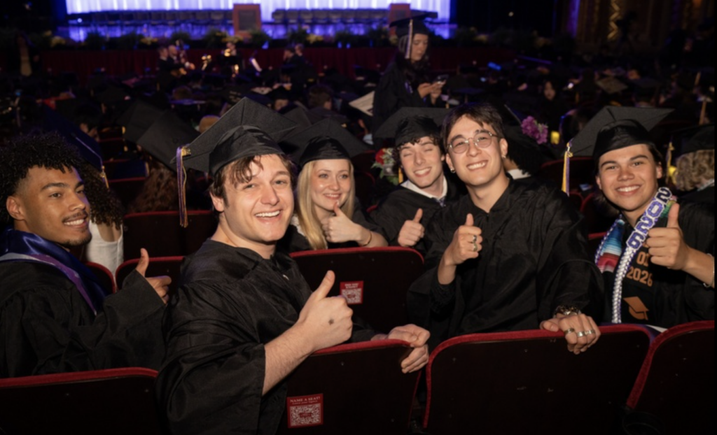 Four students pose for a photo while sitting and giving the thumbs up