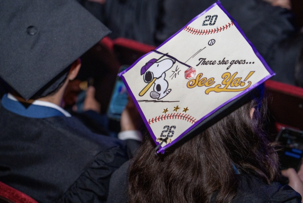 The mortar board of a cap shows Snoopy hitting a baseball