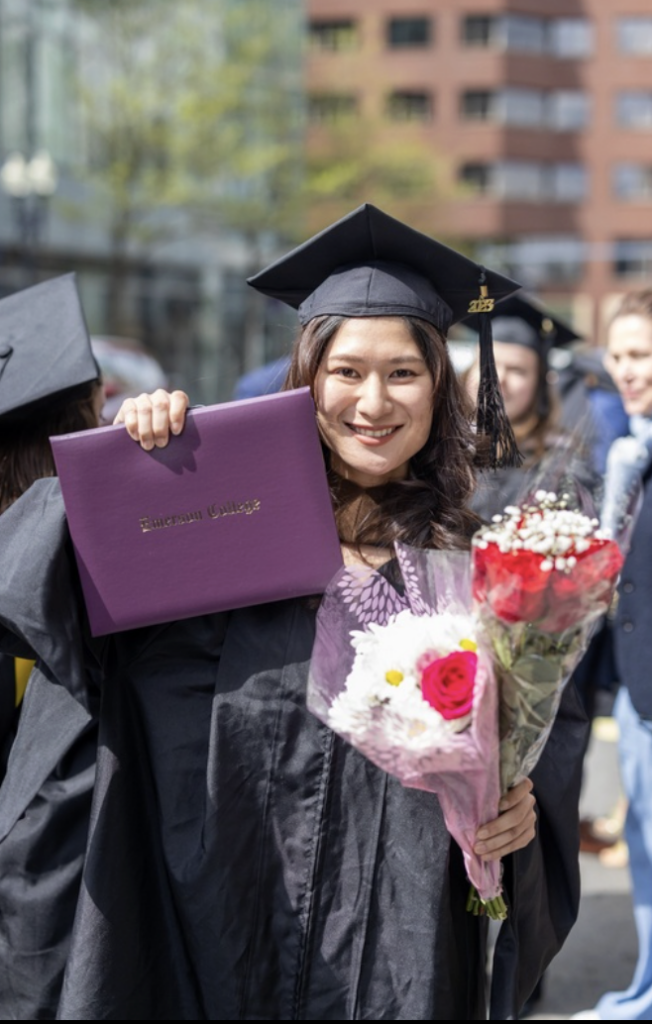 A graduate smiles while holding flowers and their diploma