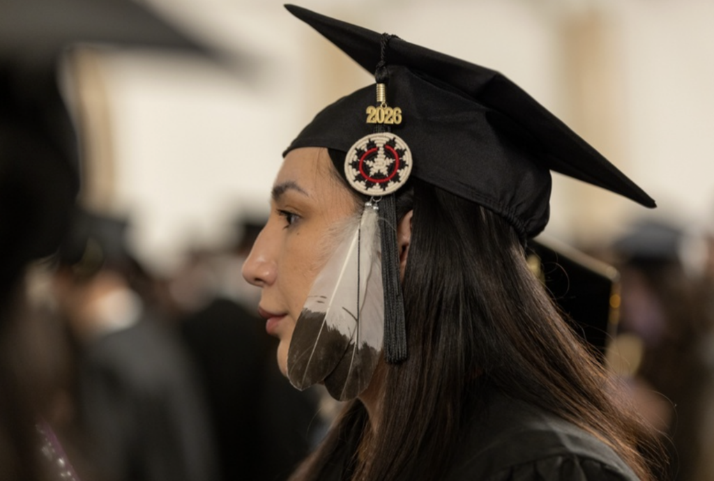 Closeup of a woman's head with two feathers and 2026 dangling from her cap
