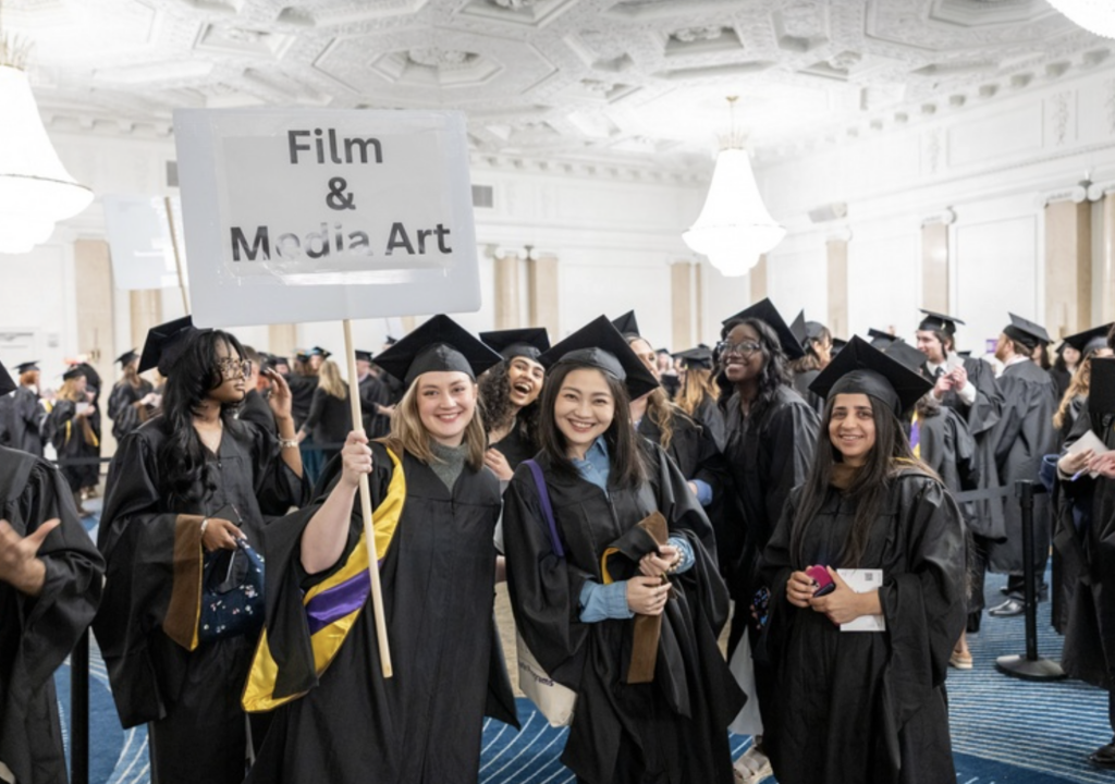 Graduates pose for photo while one holds a sign that says Film & Media Art